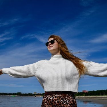 A woman with open arms and sunglasses enjoys the breeze at a beach in Tallinn, Estonia.