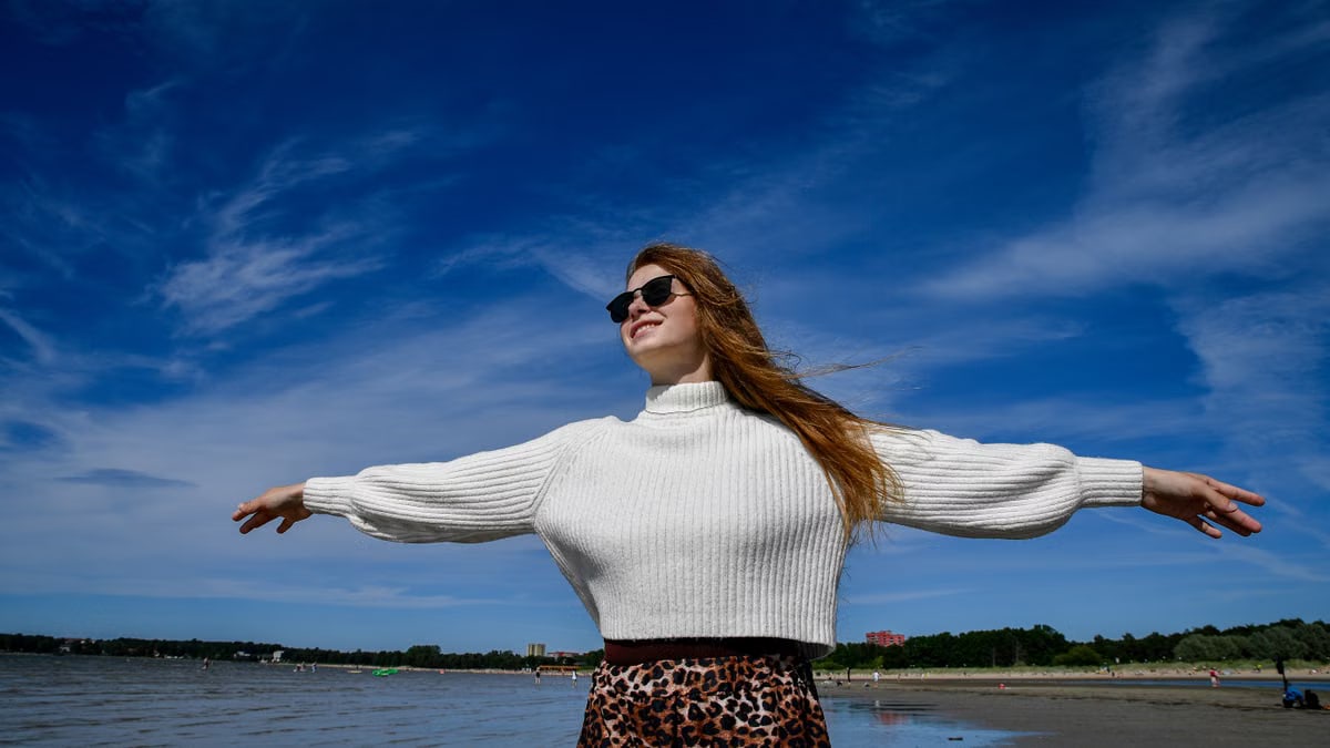 A woman with open arms and sunglasses enjoys the breeze at a beach in Tallinn, Estonia.
